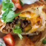 Crispy Beef and Cheese Chimichangas served with cheese sauce and garnished with lettuce and tomatoes.
