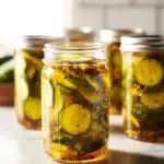 Jar of homemade bread and butter pickles with fresh cucumbers and spices.