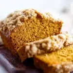 Slice of easy pumpkin bread with crumb topping on a rustic wooden table