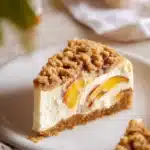 Slice of peach crumble cheesecake topped with fresh peaches and crumble