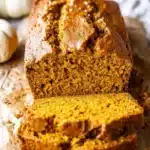 Sliced vanilla pudding pumpkin bread on a wooden table, showcasing its moist texture.