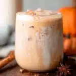 Iced Pumpkin Cream Chai Tea Latte served in a glass with whipped cream on top.