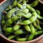 Bowl of steamed edamame with sea salt, a healthy snack option.