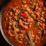 A bowl of best homemade chili topped with cheese and herbs, served with cornbread.