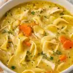 Bowl of creamy chicken noodle soup with vegetables and herbs