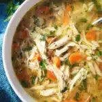 A bowl of Instant Pot lemon chicken orzo soup with fresh herbs and lemon slices