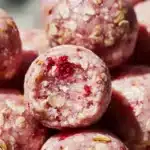 Strawberry cheesecake protein balls served on a plate with fresh strawberries