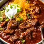 Bowl of Texas No Bean Chili with spices and garnishments on a wooden table
