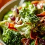 Colorful broccoli salad with nuts and dressing in a serving bowl.