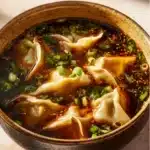 A steaming bowl of potsticker soup with dumplings and vegetables