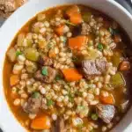 Bowl of homemade beef barley soup with vegetables and herbs